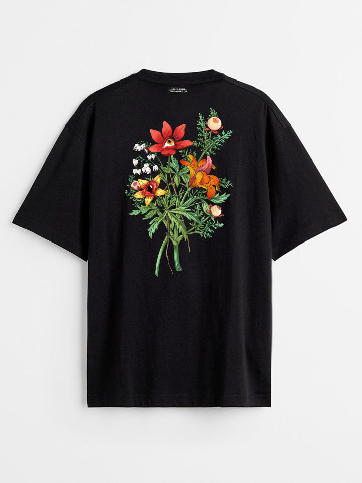 A back view of a black printed t-shirt by useless treasures. Print of an illustrated of a big bouquet of wild flowers with eyes, lips, and tongue. 