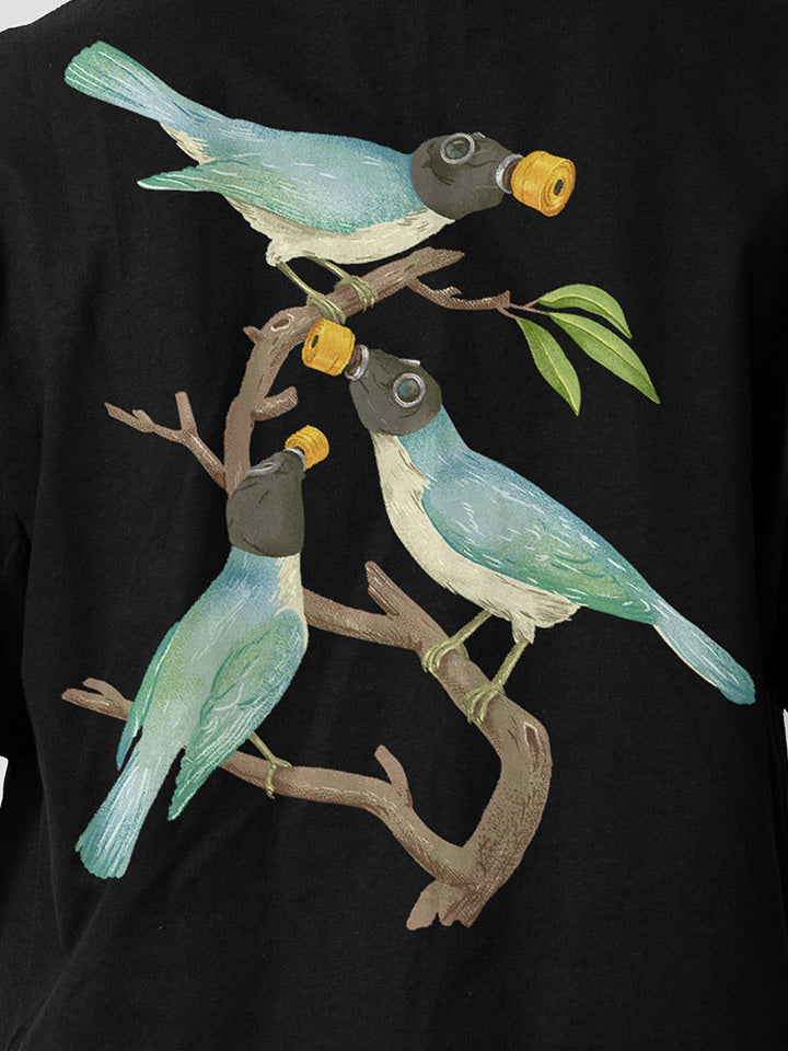 A close-up of a black printed t-shirt by useless treasures. Print of an illustration of three blue birds with gas masks sitting on a branch with a few green leaves. 