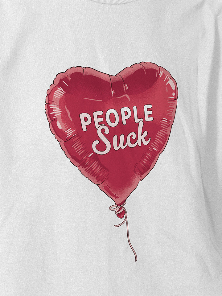 A close-up of a white printed t-shirt by useless treasures. Print of an illustrated heart shapes red balloon with the text people suck.