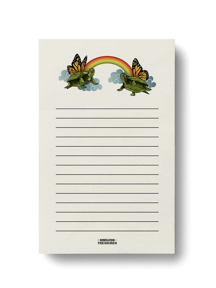 front view of a unique notepad with a humorous illustration decoration of two cute turtles with butterfly wings and a rainbow. 