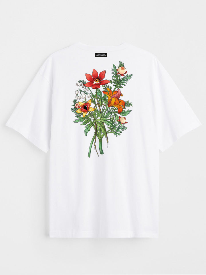 A back view of a white printed t-shirt by useless treasures. Print of an illustrated of a big bouquet of wild flowers with eyes, lips, and tongue. 