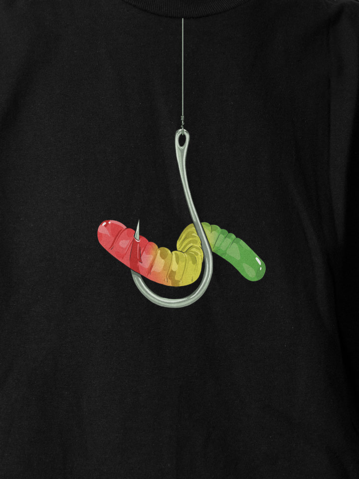 A close-up of a black printed t-shirt by useless treasures. Print of an illustration of colorful gummy warm hung on a silver hook. 
