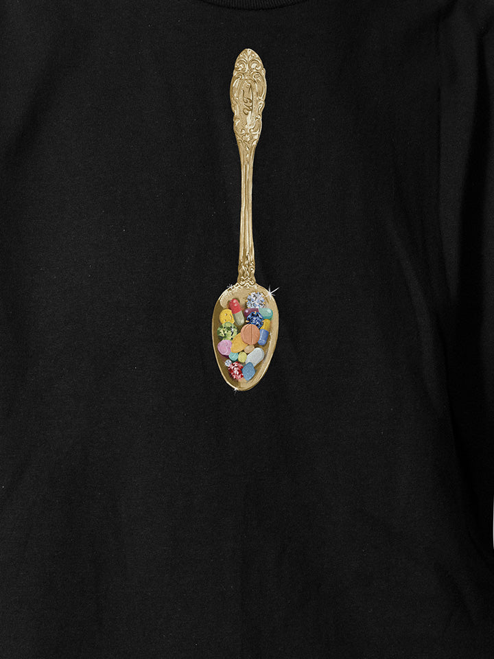 A close-up of a black printed t-shirt by useless treasures. Print of an illustrated golden spoon filled with pills and gems. 