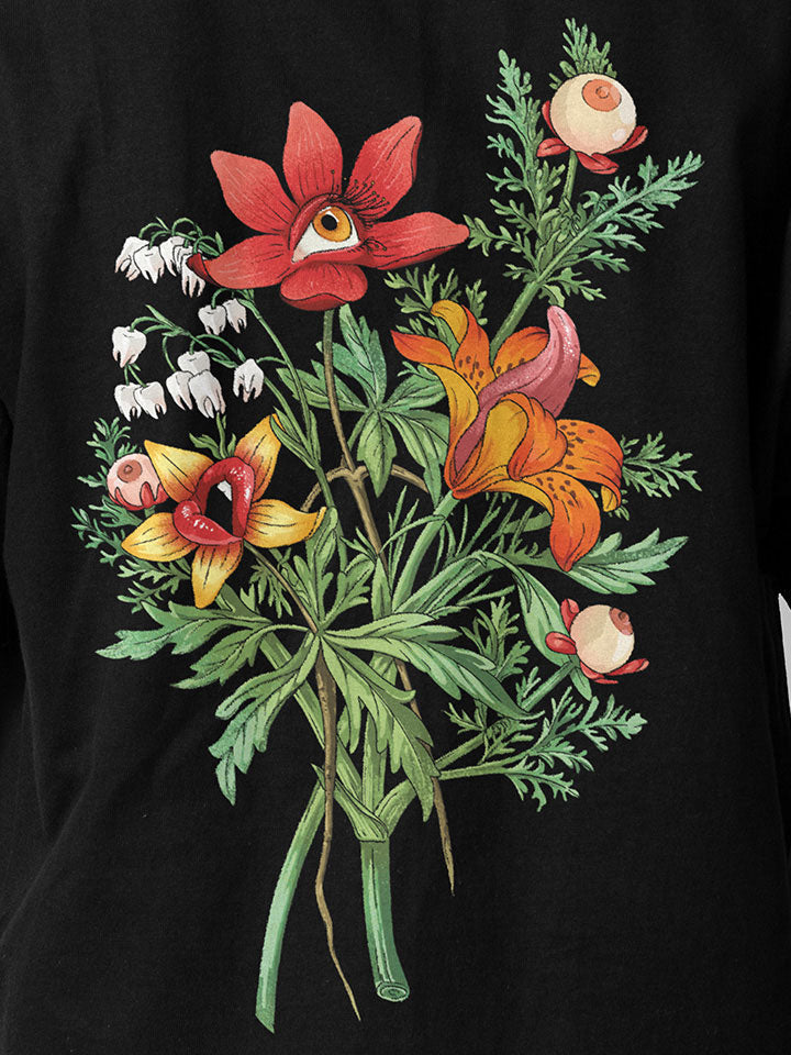 A front view of a black printed t-shirt by useless treasures. Print of an illustrated of a big bouquet of wild flowers with eyes, lips, and tongue. 