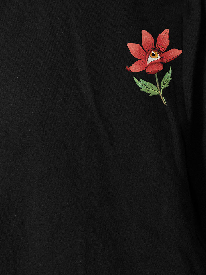 A close-up of a black printed t-shirt by useless treasures. Print of an illustrated red flower with a yellow eye. 