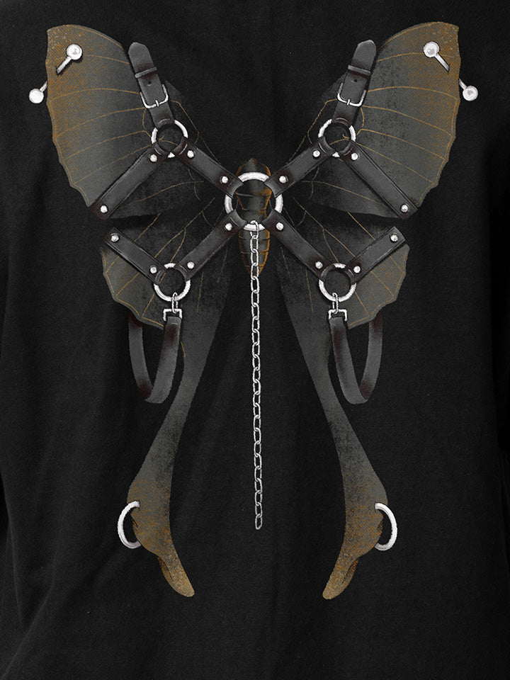 A close-up of a black printed t-shirt by useless treasures. Print of an illustrated black moth with leather gear and silver chains​ and piercings. 