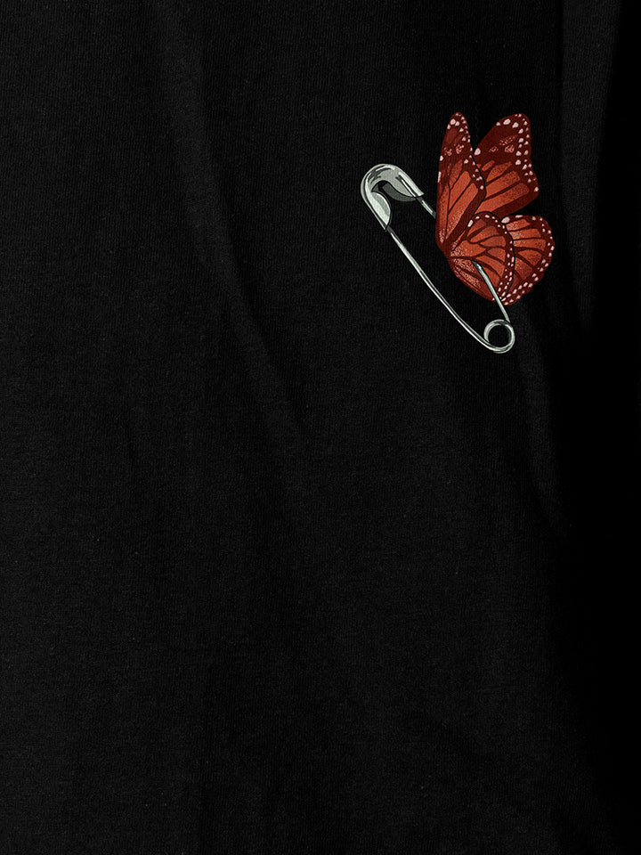 A close-up of a black printed t-shirt by useless treasures. Print of an illustrated ​butterfly with a safety pin body
