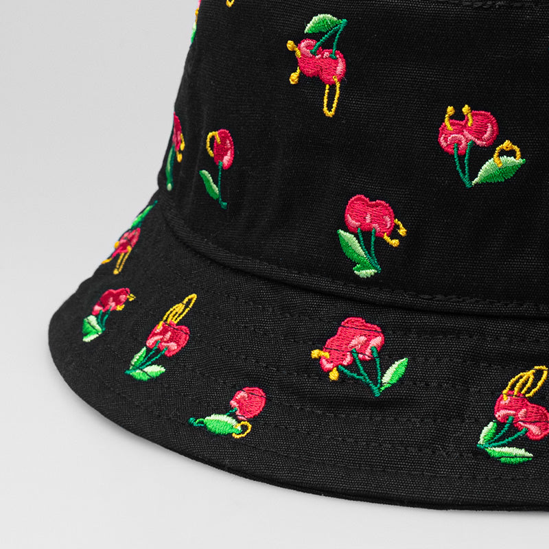 A black On & Off x Useless Treasures bucket hat with small embroideries of cherries with piercings and earrings; on one side of the hat is also a black label of On& Off logo- designed by useless treasures.