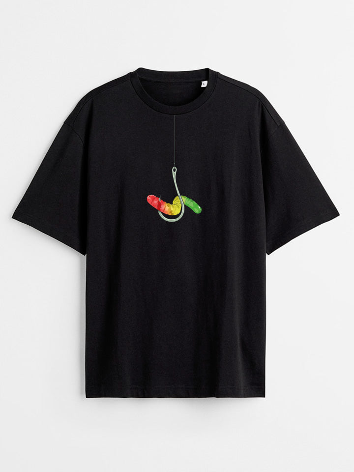 A Black oversize printed T-shirt. Short sleeve Shirt with a print called "temptation" of a silver hook holding a colorful gummy warm. Surreal illustration by useless treasures. Organic cotton, loose fit.